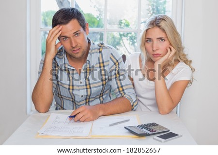 Worried young couple with financial documents and calculator sitting at home