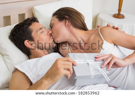 Relaxed young couple kissing with gift box in hand in bed at home