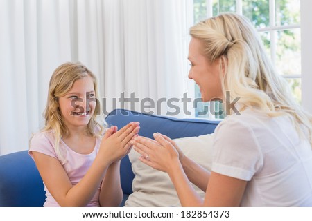Happy cute girl playing clapping game with mother on sofa at home