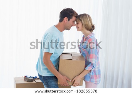 Side view of a smiling young couple carrying cardboard box in new house