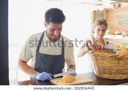 Portrait of a smiling young waiter with croissant at the coffee shop counter