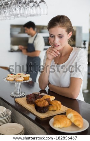 Thoughtful young female cafe owner with sweet food at counter