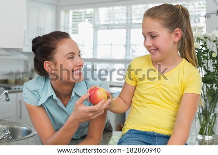 Happy girl giving apple to mother in kitchen