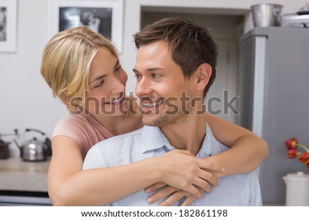 Close-up of a smiling young woman embracing man from behind in kitchen at home