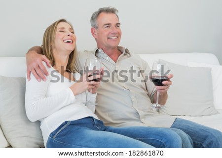 Happy relaxed couple with wine glasses sitting on sofa at home