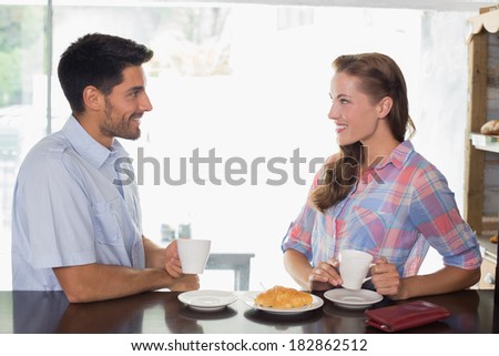 Side view of a smiling young couple with coffee and croissant at the coffee shop