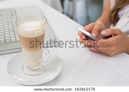 Close-up of a drink with hands using mobile phone on table in the coffee shop