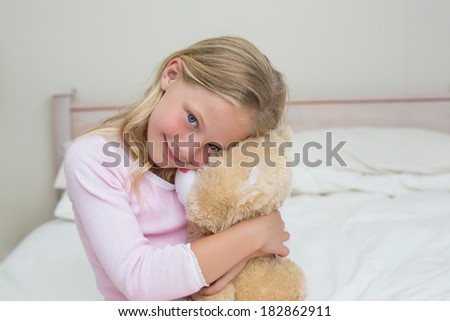 Portrait of a young girl embracing stuffed toy in bed at home