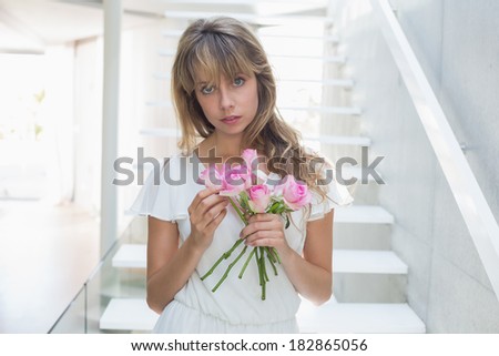 Portrait of a beautiful sad young woman with flowers standing on stairs at home