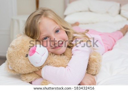 Close-up portrait of a young girl resting in bed with stuffed toy at home