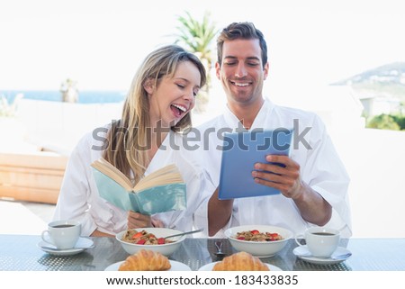 Cheerful young couple with book and digital tablet on breakfast table at home