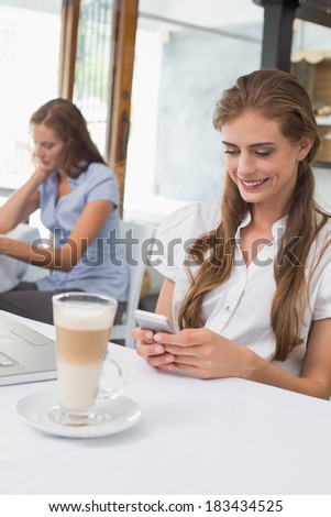 Smiling young woman using mobile phone in the coffee shop