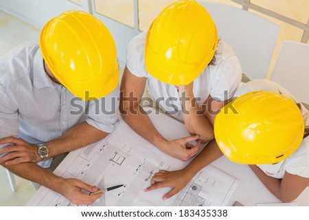 Top view of architects in yellow helmets working on blueprints at the office