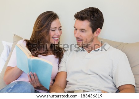 Loving relaxed young couple reading book on couch at home