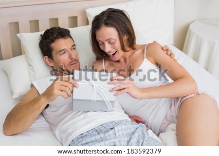 Relaxed young couple with gift box lying together in bed at home