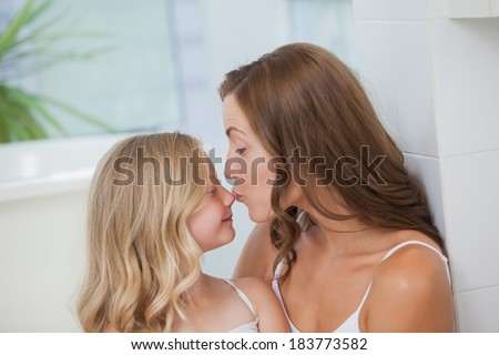 Close-up side view of a mother kissing on daughter\'s nose at home