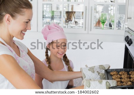 Yung girl looking at mother remove cookies from the oven in the kitchen