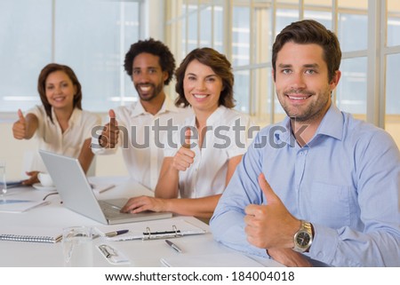 Portrait of happy business people gesturing thumbs up in meeting at the office