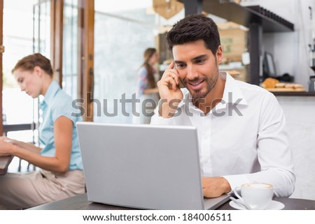 Portrait of a happy young man using laptop and mobile phone in the coffee shop