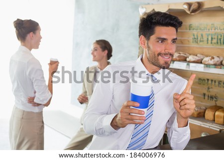 Businessman with coffee sipper at the counter with colleagues behind in office cafeteria