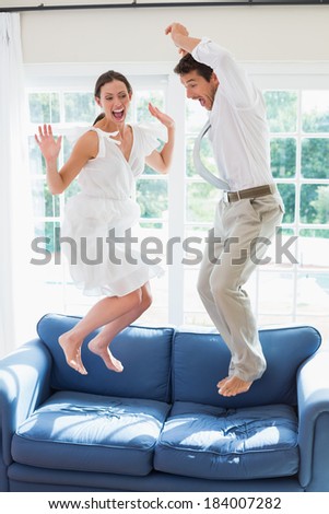 Side view of a cheerful young couple jumping on couch at home
