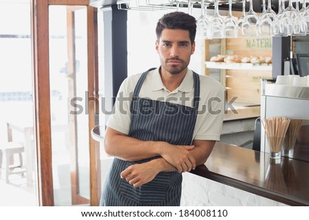 Portrait of a serious confident young waiter standing at the cafe counter