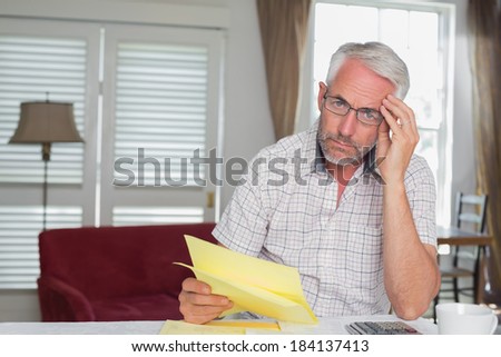 Serious mature man sitting with home bills and calculator at table