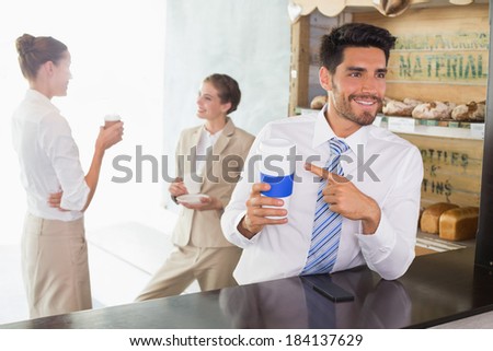 Businessman with coffee sipper at the counter with colleagues behind in office cafeteria