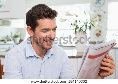 Smiling young man reading newspaper at home