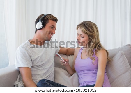 Relaxed young couple listening music with mobile phone on couch at home