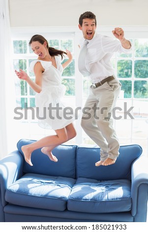 Side view of a cheerful young couple jumping on couch at home