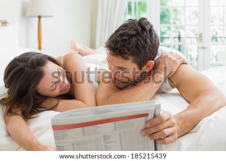 Relaxed young couple reading newspaper in bed at home