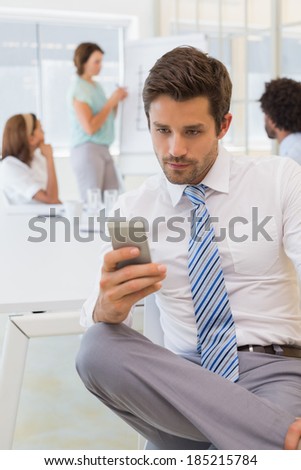 Serious businessman text messaging with colleagues in meeting in background at the office