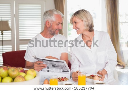 Mature couple reading newspaper while having breakfast at home