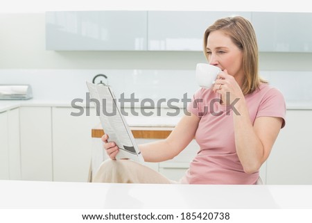 Relaxed woman reading newspaper while having coffee in the kitchen at home