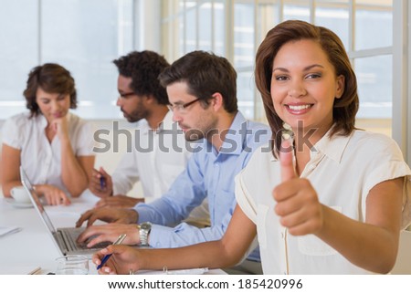 Portrait of a smiling businesswoman gesturing thumbs up with colleagues in meeting at the office