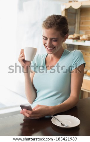 Smiling young woman drinking coffee while using mobile phone at counter in the coffee shop