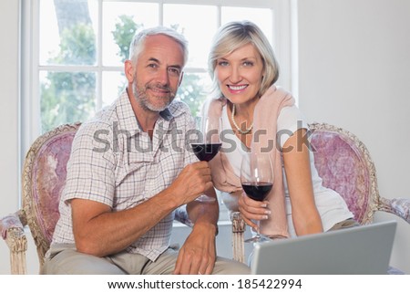 Portrait of a smiling relaxed mature couple with wine glass using laptop at home