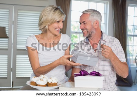 Happy woman giving a gift box to smiling mature man at home
