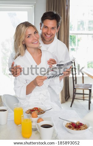 Portrait of a happy young couple reading newspaper while having breakfast at home