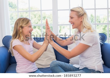 Happy mother and daughter playing clapping game on sofa at home