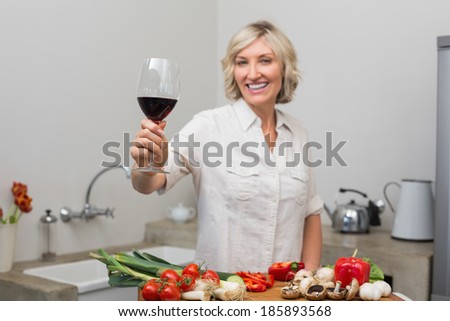 Portrait of a happy mature woman with vegetables and wine glass in the kitchen at home
