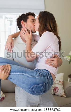 Loving young man carrying woman as he kisses her at home