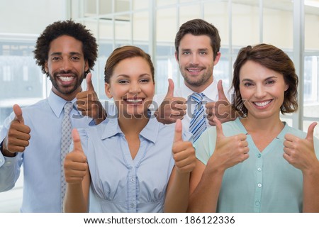 Portrait of young business colleagues gesturing thumbs up in the office