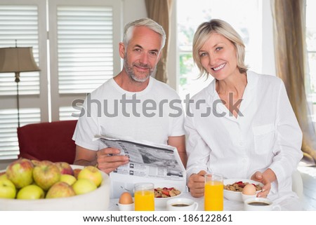Mature couple reading newspaper while having breakfast at home