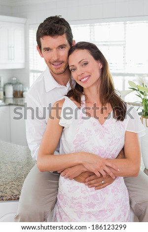 Portrait of a loving young man embracing woman from behind in the kitchen at home