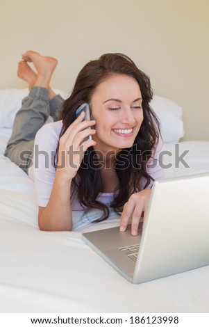 Happy woman on call while using laptop in bed at home