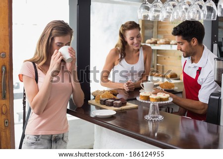 Smiling woman drinking coffee with friend and male barista at counter in the coffee shop