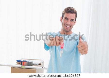 Portrait of a young man holding out new house key while gesturing thumbs up