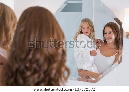 Portrait of a happy mother and daughter looking at bathroom mirror in the house